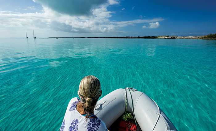 Blonde female at the front of a small boat overlooking clear blue waters.