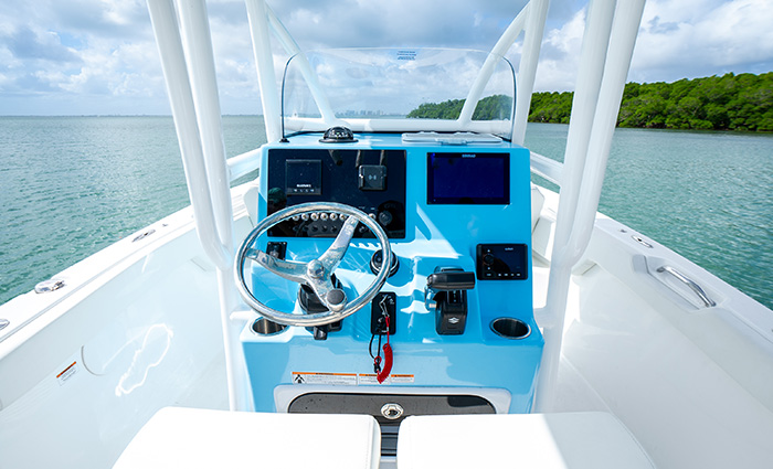 The helm of a white vessel out on the water with green trees along the shoreline in the background.