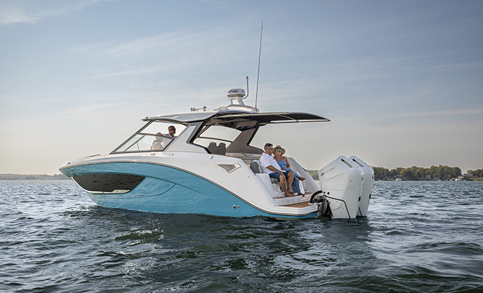 Four adults aboard a large white and blue vessel with double engines on the water at sunset.