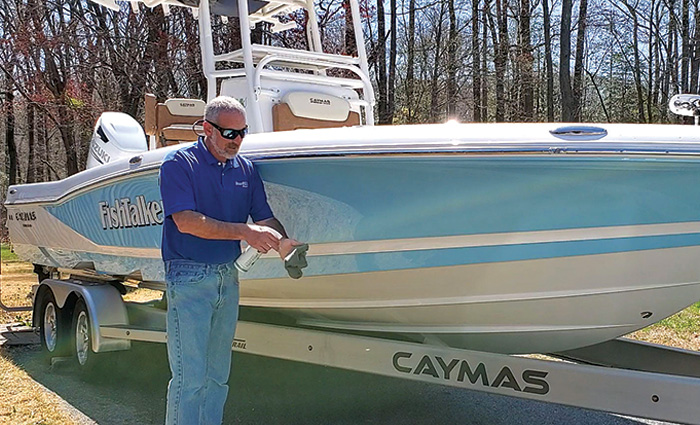 Adult male in a blue polo and jeans adding a ceramic coat to his white and blue vessel.