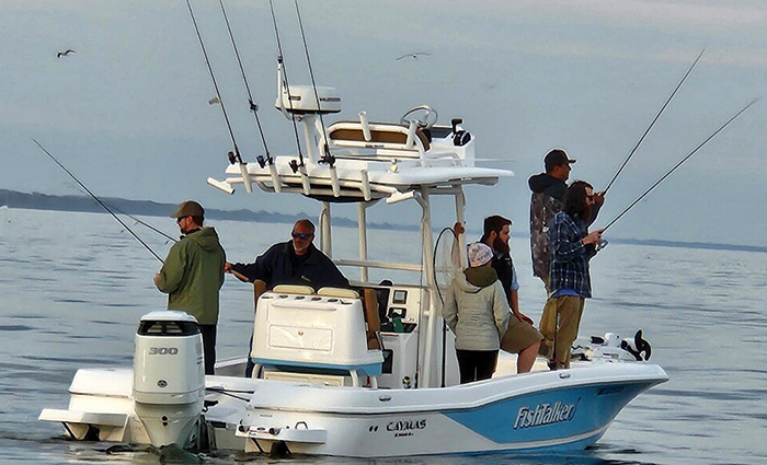 Six adults fishing off a white and blue vessel on open waters at dusk.