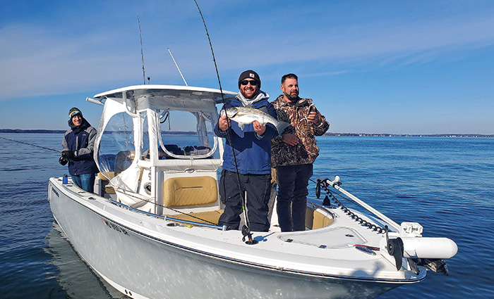 Three adult males in a small white fishing boat proudly displaying a catch.