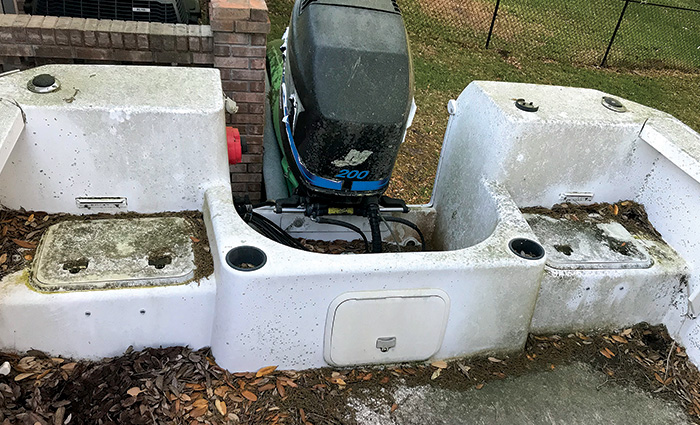 Worn, weathered and unkept back of a boat with black motor.