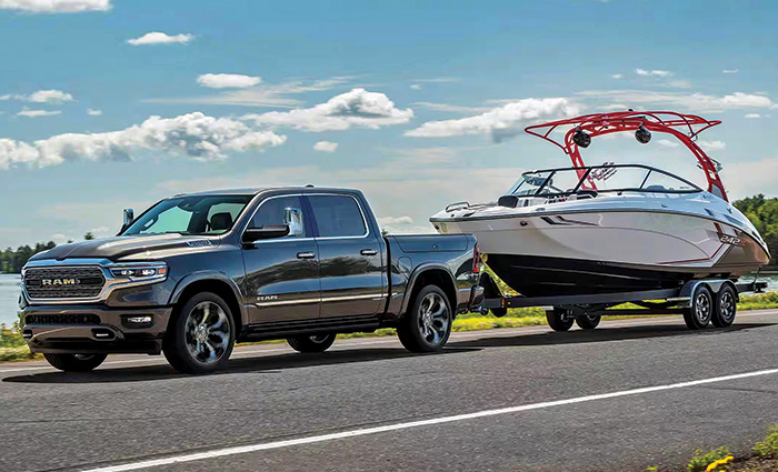 Black Dodge Ram truck hauling a white speed boat on a trailer.