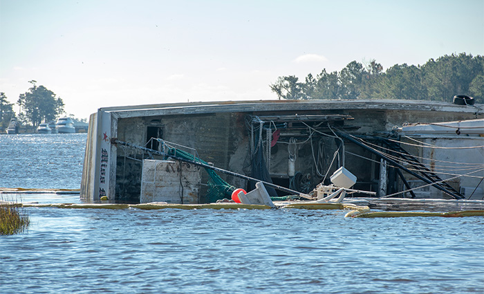 A capsized boat surrounded by debris in open water on a sunny day.