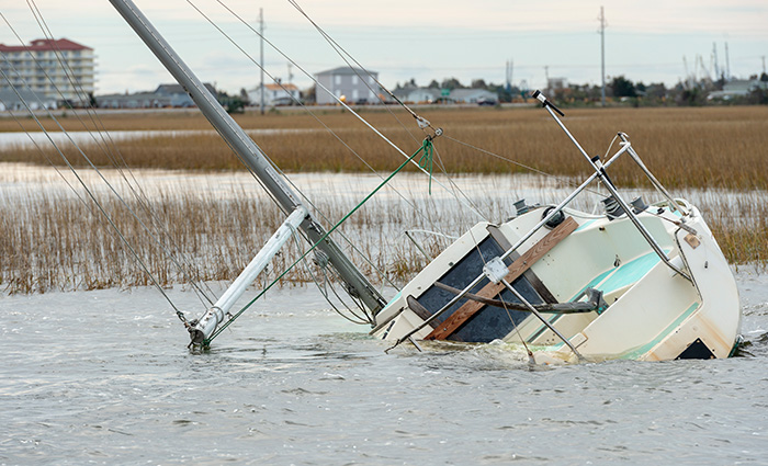 A white sailboat capsized on the shore in shallow water.