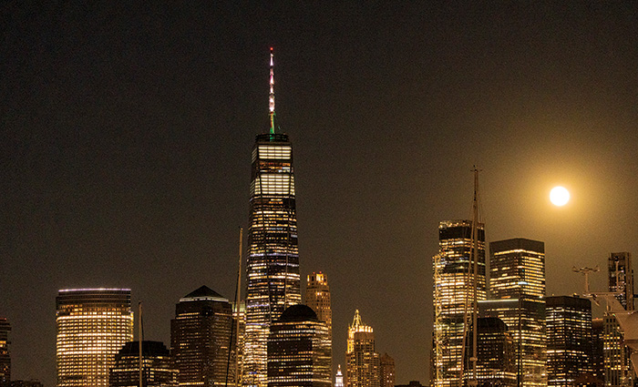 A number of skyscrapers illuminated by a full moon at night.