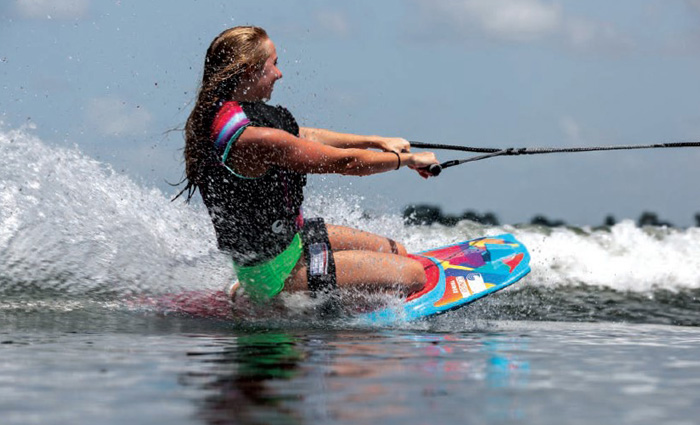Young adult female wearing a black life jacket water wakeboarding on a sunny day.
