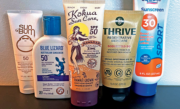 Five bottles of various sunscreen lined up next to each other on a black table.