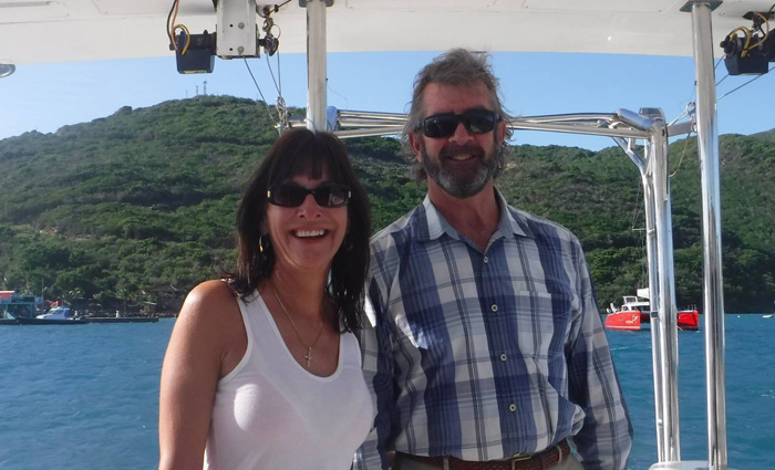 Adult female wearing a white tank top and black sunglasses next to bearded adult male wearing a plaid shirt and black sunglasses.