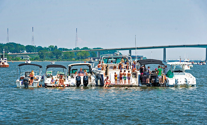 Six vessels anchoring together with numerous young adults onboard enjoying sunny weather.