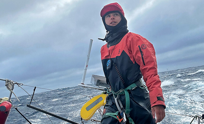 Young adult female wearing a red and black rain suit on the back of a vessel in open waters.