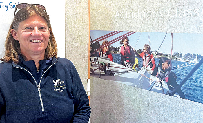 Adult Caucasian female wearing a navy quarter zip jacket posing next to a photo of kids on a boat. 