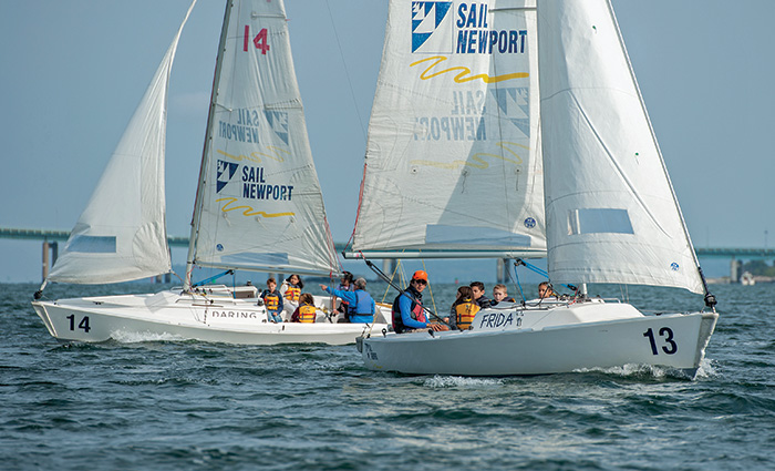 Two white sailboats with a mixture of adult and youth passengers out on open waters during a clear, sunny day.