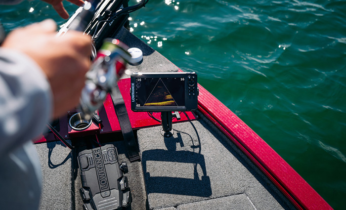 A small sonar device connected to a red fishing boat on open waters while an adult casts a line to fish.