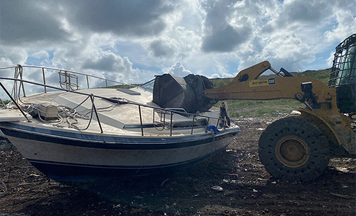 Large yellow bulldozer destroying a derelict white and blue boat.