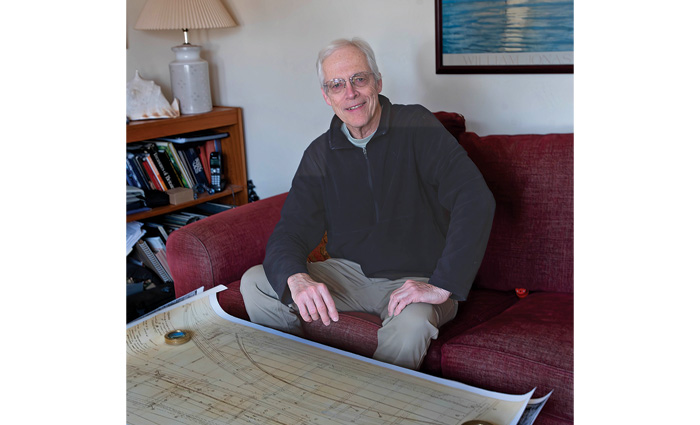 Elderly male wearing a dark sweater and khaki pants sitting on a red couch.