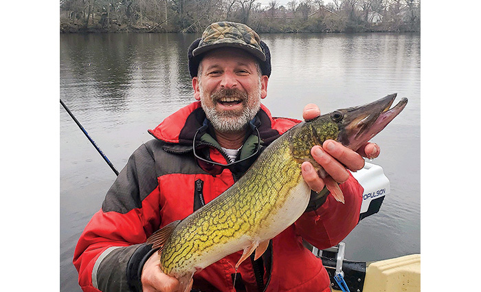 Adult male wearing a camouflage hat and red and black float coat proudly displaying a fish caught.