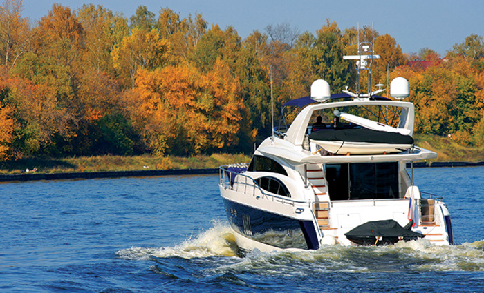 Large white and black vessel on open waters with fall foliage in full display.