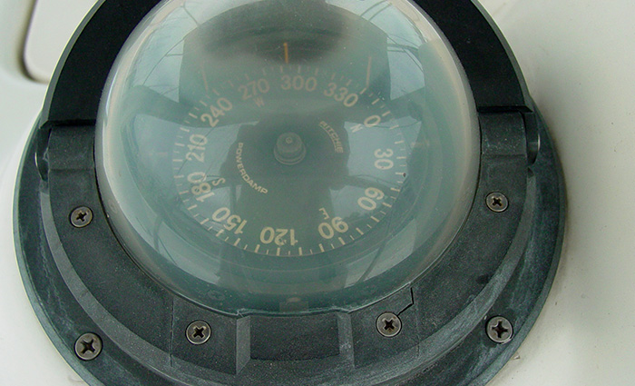 Cloudy and damaged black boat compass with white numbers and letters.