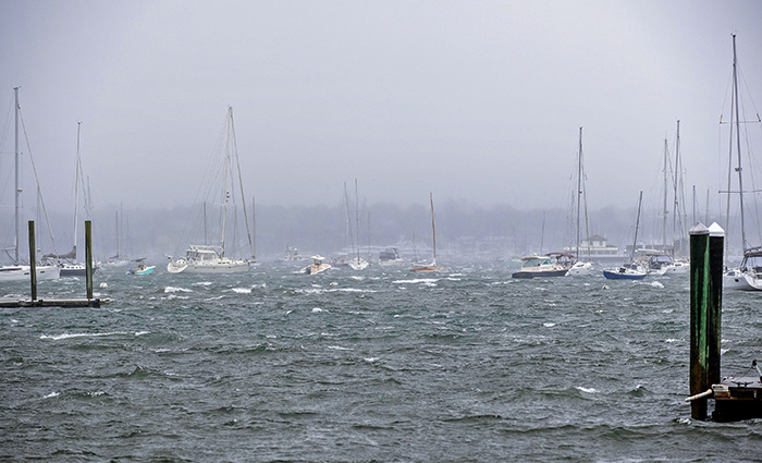 Numerous sailboats out on choppy waters during overcast and inclement weather.