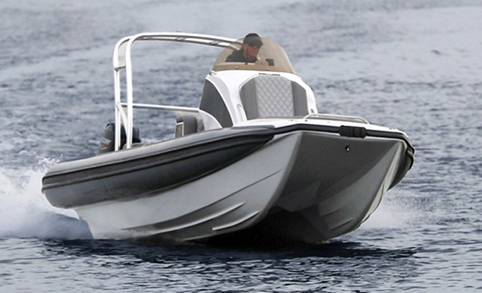 Adult male wearing a gray hat navigating a small white and black vessel on open waters.