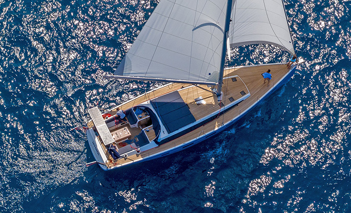 Ariel view of a white sailboat on clear blue waters during a sunny day.