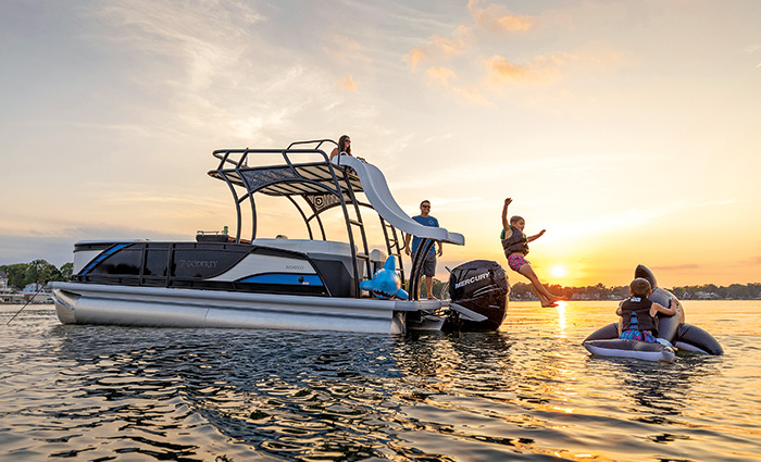 Family enjoying a slide atop a pontoon boat on the water at sunset.