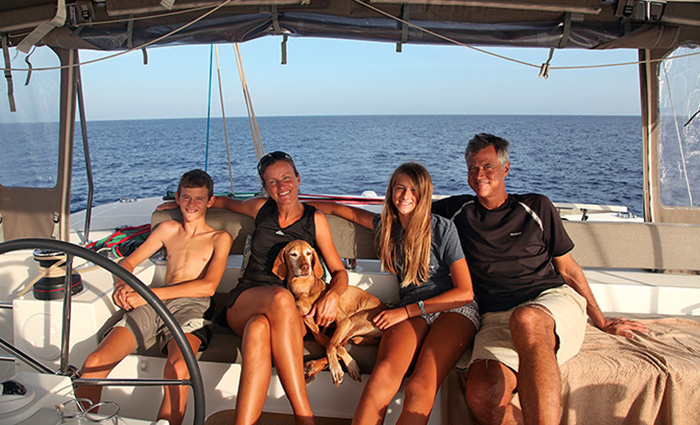Family of four posing for a photo with brown dog aboard a white vessel at sunset.