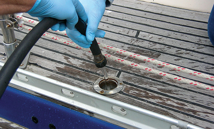 Two hands wearing blue rubber gloves holding a hose using water to clean a holding tank.