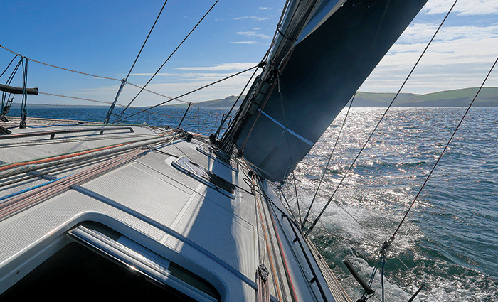 View from aboard a sailboat leaning to the right and cruising through open waters on a sunny day.