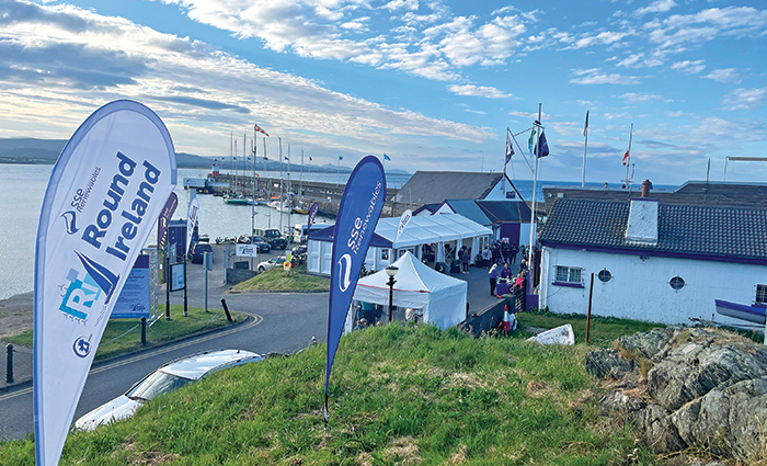 Winding road with white houses and white pop-up tents off the water with fluffy clouds above.