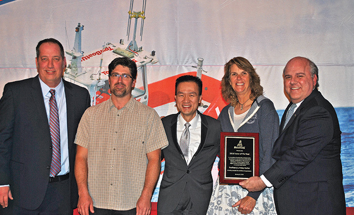 Four adult males and an adult female posing for a group photo while one holds a plaque. 