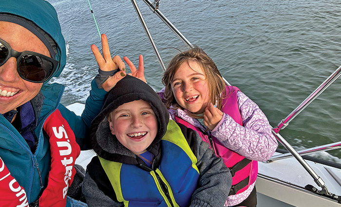 Adult female with two children, one little boy and a little girl, posing for a selfie on a boat on the water.