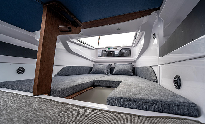 Interior cabin of a boat with a U shaped gray seating area with gray pillows and a wooden beam.
