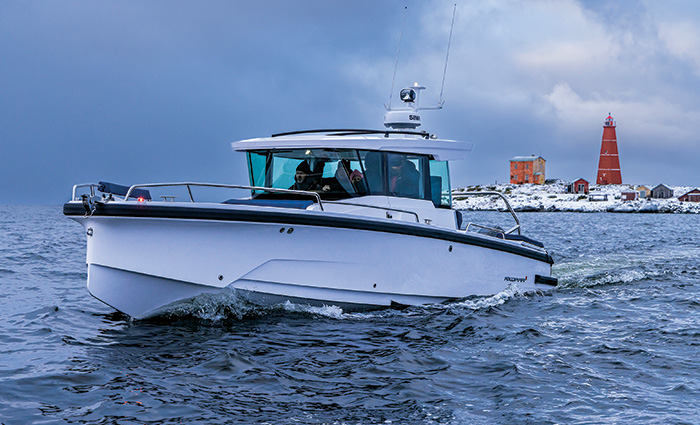 A white boat cruising on open waters with cloudy skies above and a red lighthouse and snow covered shore in the background.