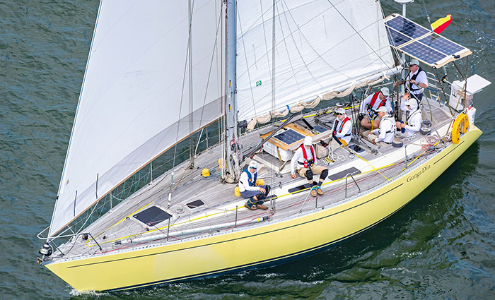 Handful of adult males wearing white hats and white clothing aboard a yellow and white sailboat with large solar panels out at sea.