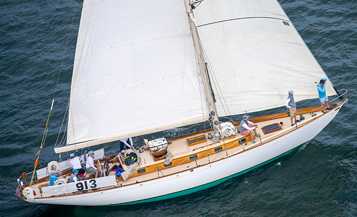 Aerial view of a white and teel sail boat with white sails out on open waters.