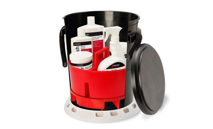 Black bucket with black lid on the side exposing a red bucket with handle and various white bottles of cleaning materials inside.