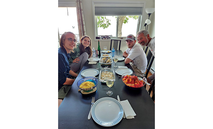 Three middle aged adults, two male and one female, and a senior adult male posing for a photo while at a black dinner table.