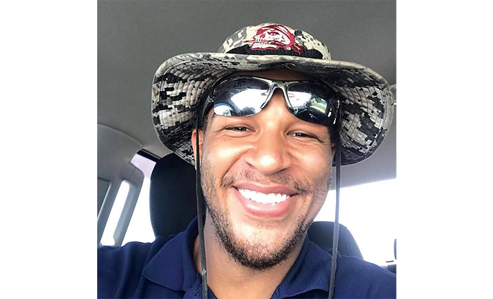 Young adult African American male wearing a bucket hat and navy shirt smiling for a selfie. 