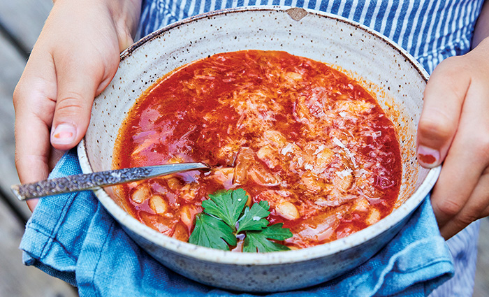 Young female in a blue and white shirt holding a bowl of tomato soup.