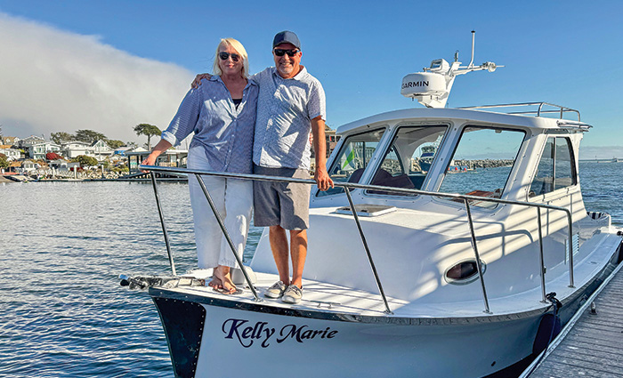 Senior adult male with arm around senior adult female standing on the bow of a white boat.