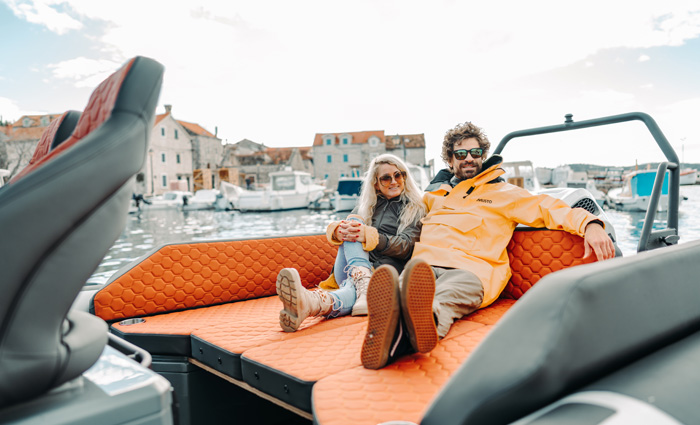 Adult male and adult female sitting on a orange filler cushion on the bow of a boat out on the water.