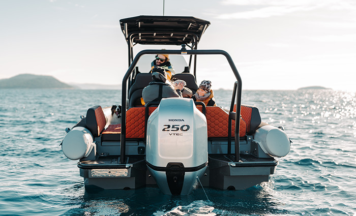 View from behind a silver boat on the water showcasing a fiberglass hull and large motor.