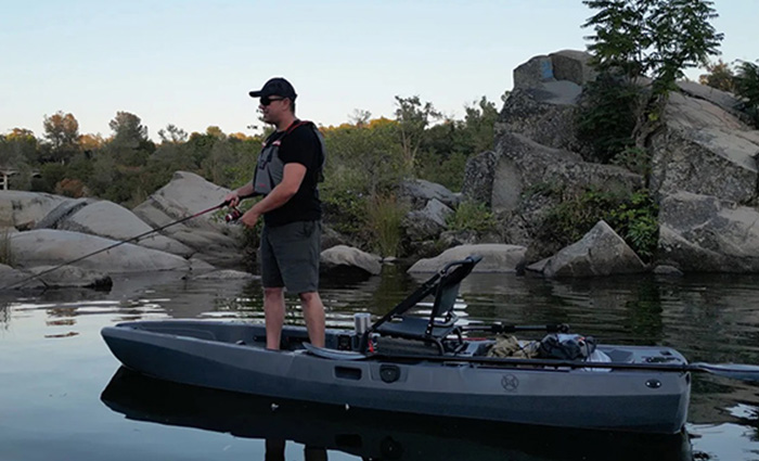 Adult male standing and fishing on kayak at sunset.