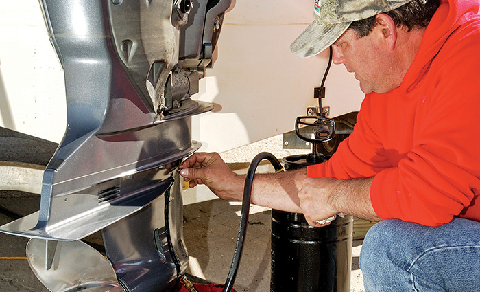 Adult male wearing a red hooded sweatshirt, jeans and a hat working on a boat engine. 