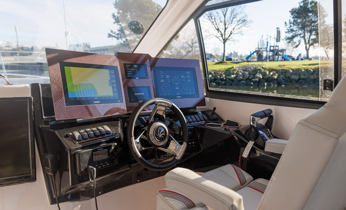 Vessel helm featuring dual chart plotter, black joystick, silver and black steering wheel and white and tan leather chair.