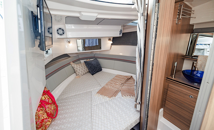 Boat cabin displaying white sleeping area with windows next to a marine toilet and shower.