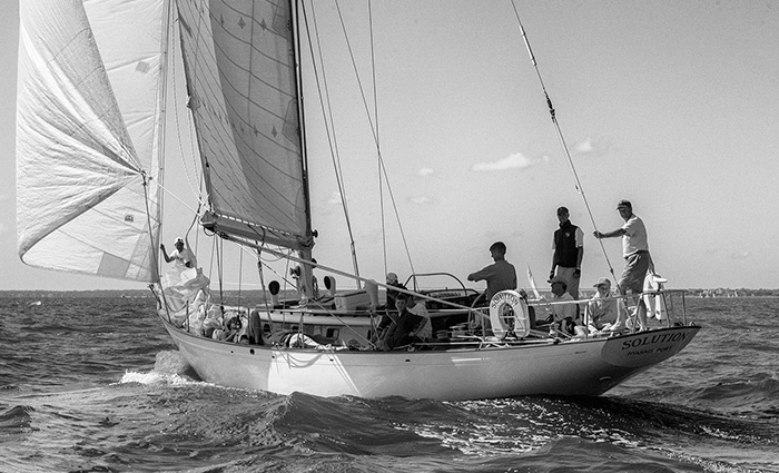 Black and white photo featuring a group of men aboard a large sailboat on open waters.